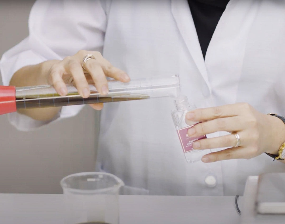 person wearing a lab coat pours liquid from test tube